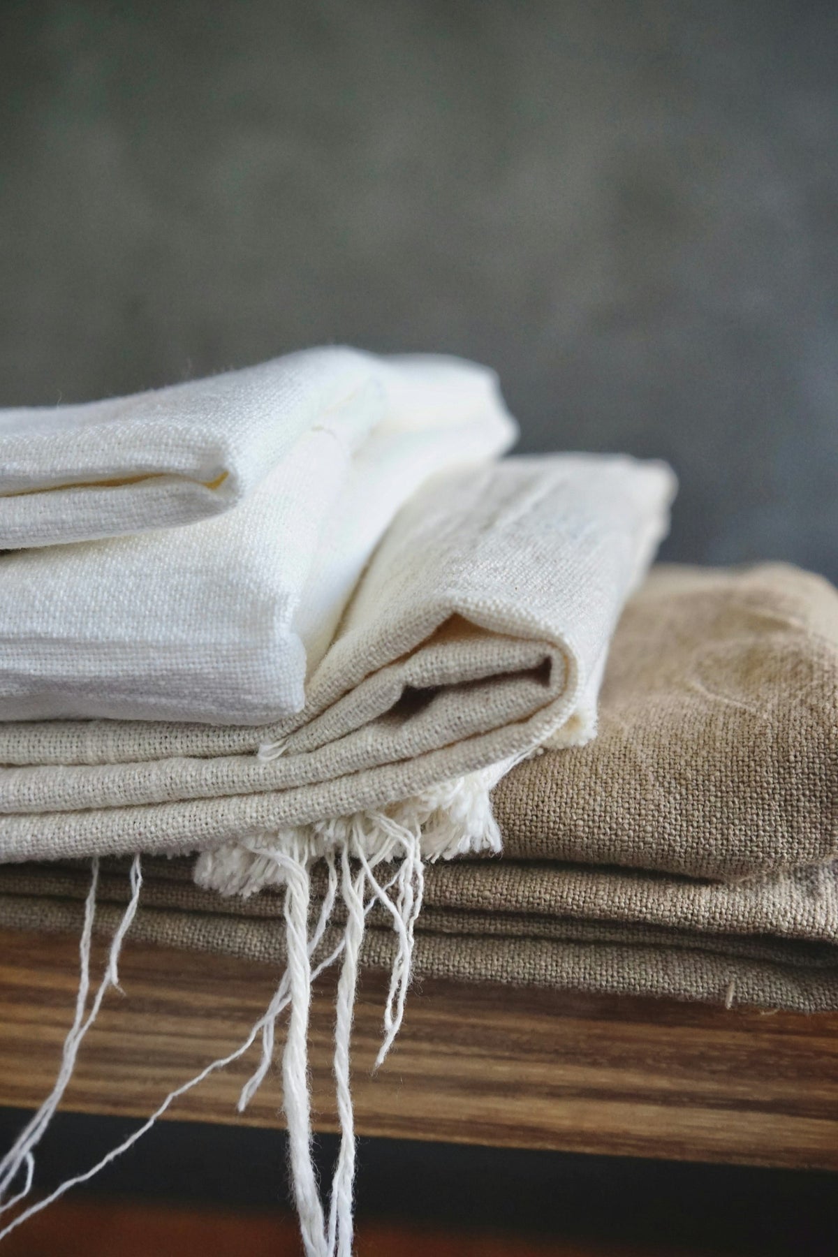 Servilletas de lino blanco con flecos, dobladas sobre una mesa de madera.