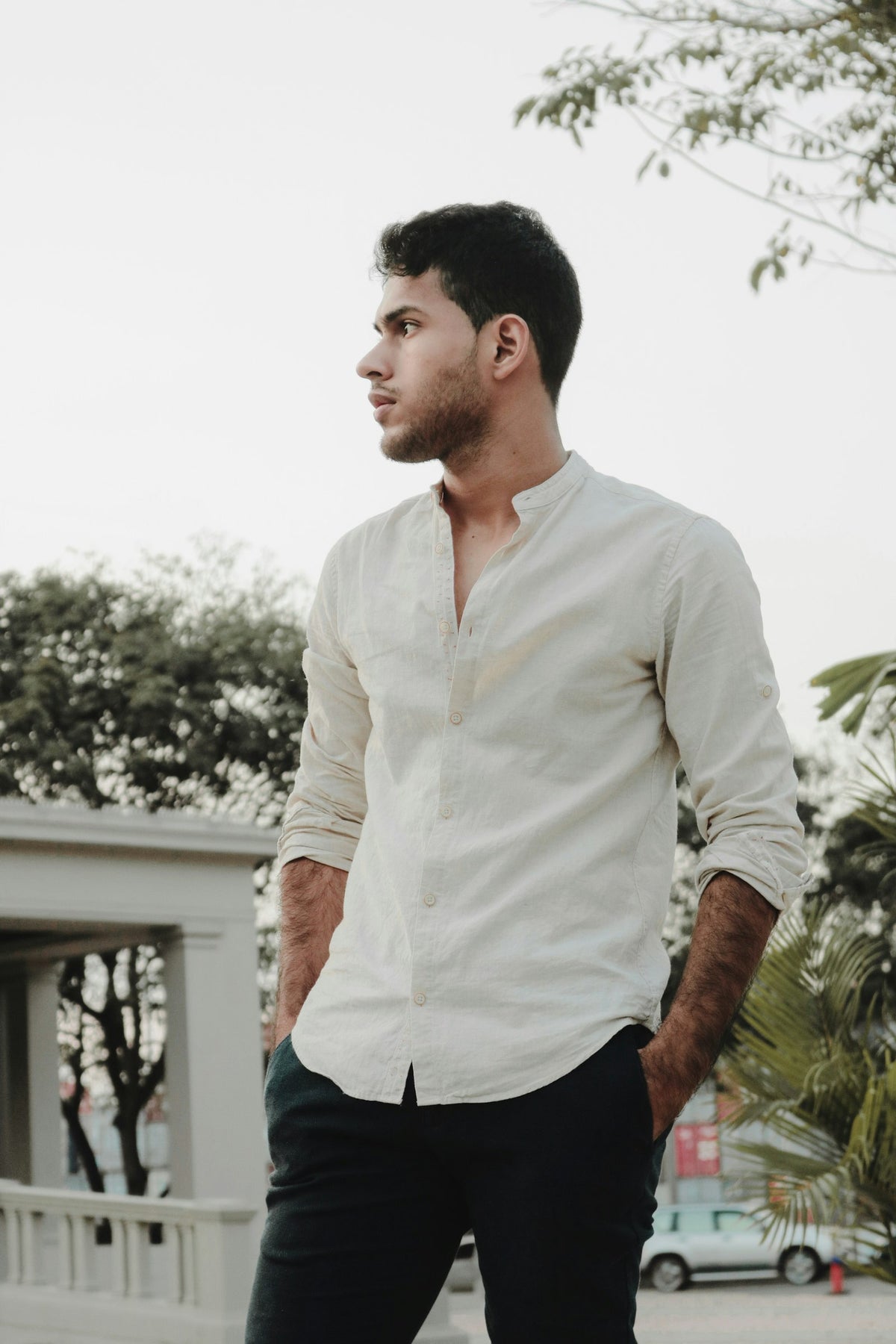 Hombre con camisa blanca de lino de manga larga, entre plantas, con luz de mañana.