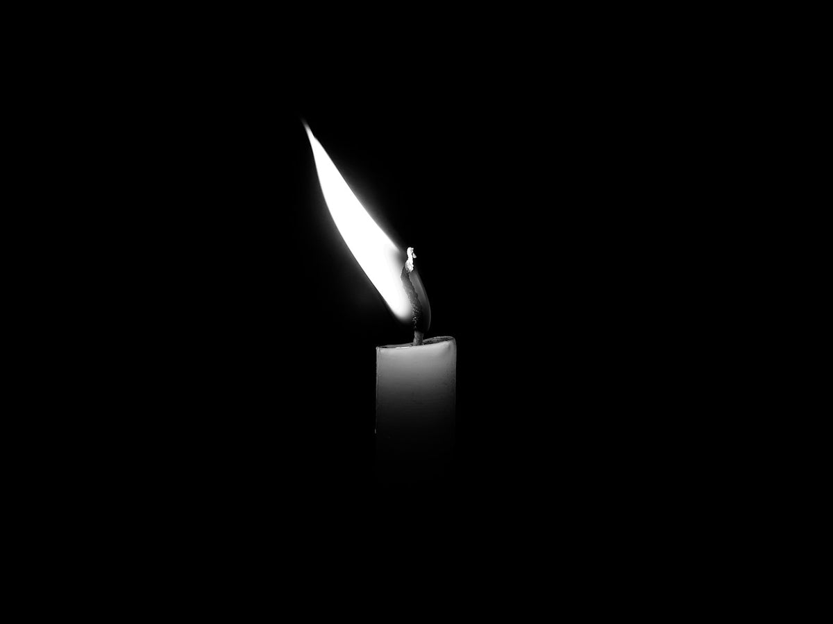 Flama de una vela de cera encendida en la oscuridad.