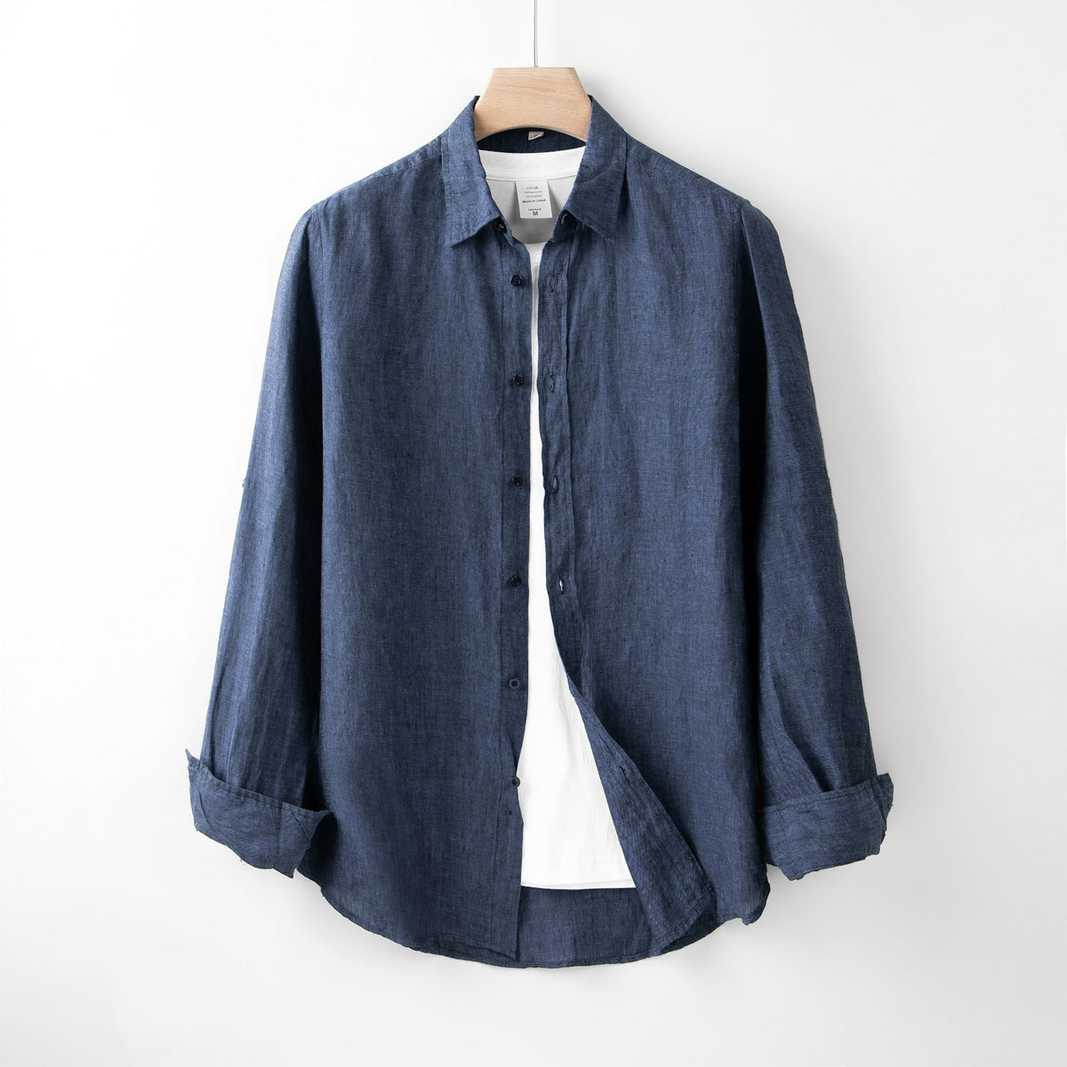 Camisa azul de algodón colgada de un gancho, en una pared blanca.