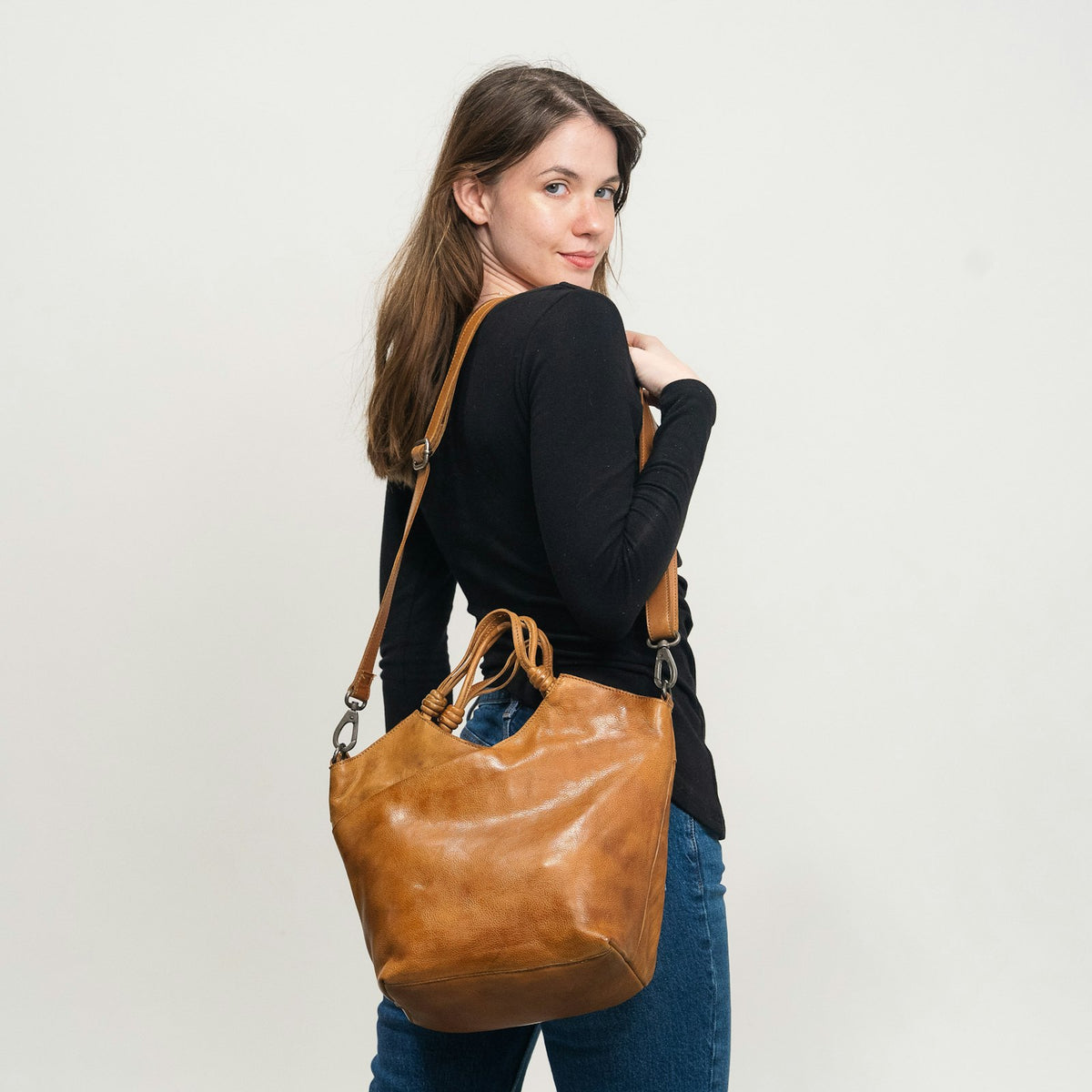 Mujer de espaldas con una bolsa de piel color coñac al hombro.