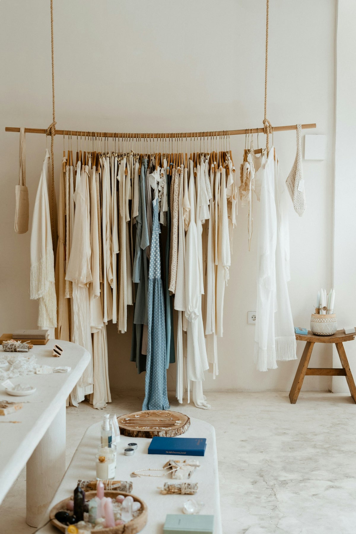 Prendas de lino en blanco, crudo y azul, colgadas de una vara de madera en un cuarto encalado.