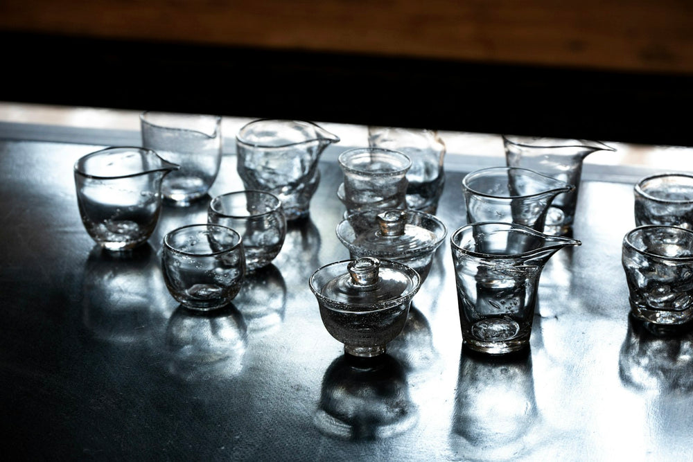 Vasos chicos de vidrio soplado, juntos sobre una mesa que los refleja.