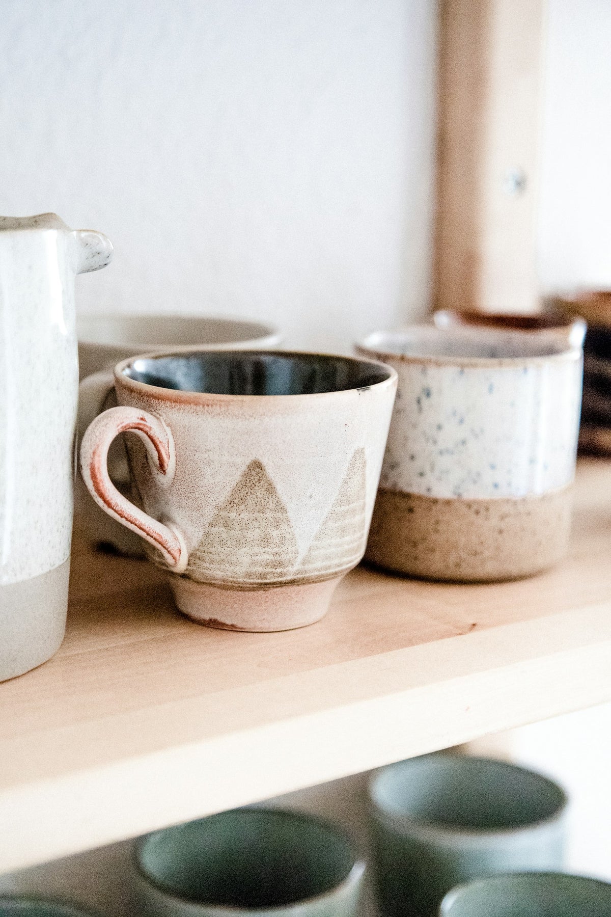 Dos tazas de cerámica moteada, una con asa rosa, en una repisa de madera.