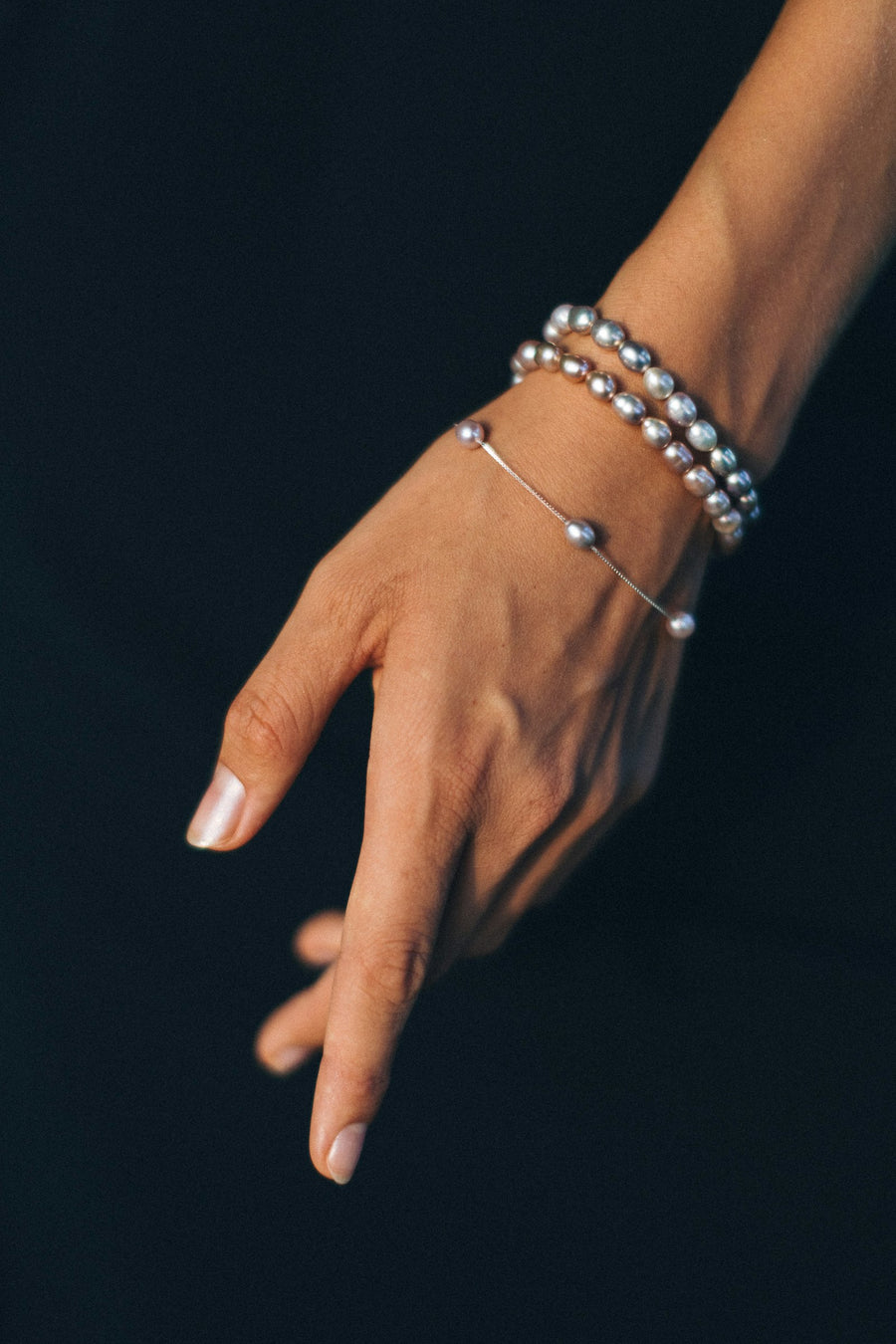 Mano con pulseras de cuentas de plata, sobre un fondo azul noche.