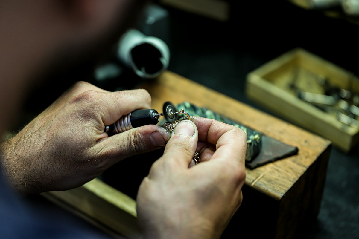 Manos de joyero trabajan un anillo con piedra verde sobre el banco.