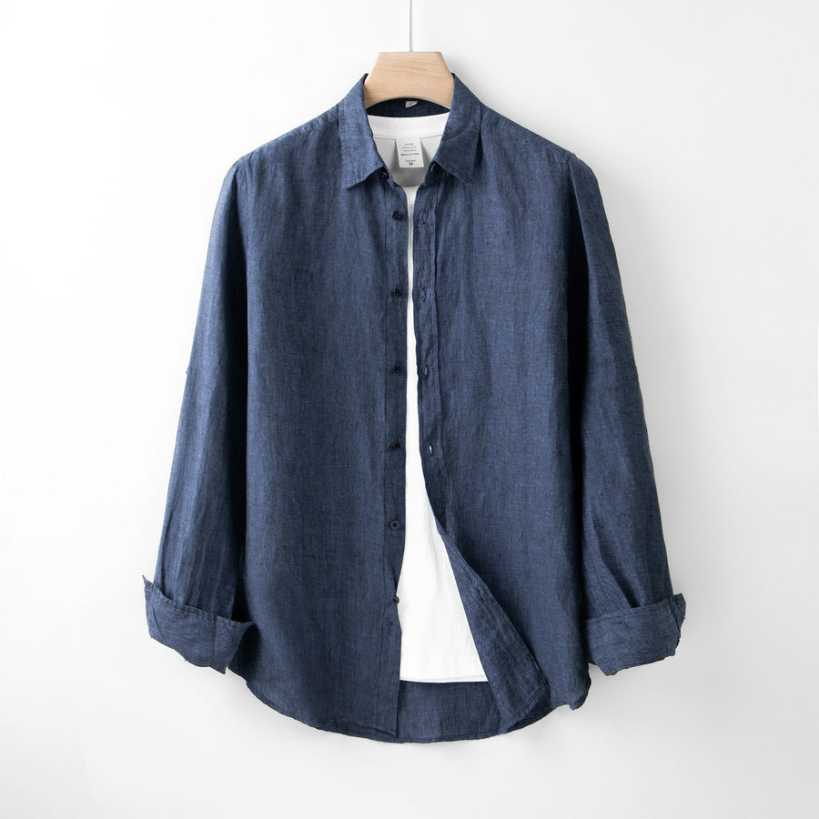 Camisa azul de algodón colgada de un gancho, en una pared blanca.