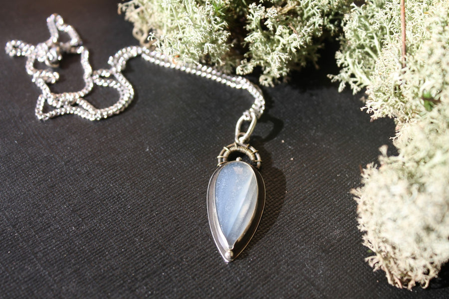 Collar de plata con una gota de piedra luna, sobre una superficie oscura.