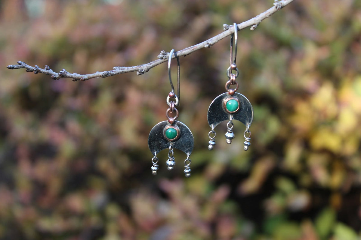 Aretes de plata con piedras verdes, colgados de un hilo.