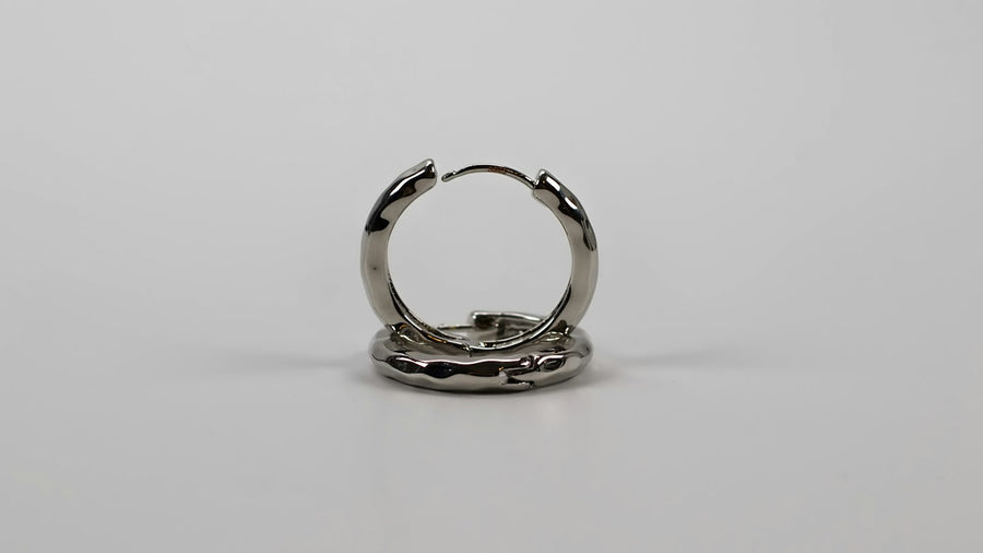 Arracada de plata martillada, de pie sobre un fondo gris claro.