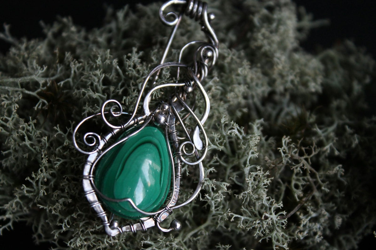 Dije de plata calada con una malaquita verde, colgado de una cadena fina.