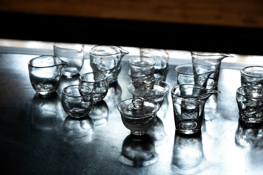 Vasos chicos de vidrio soplado, juntos sobre una mesa que los refleja.