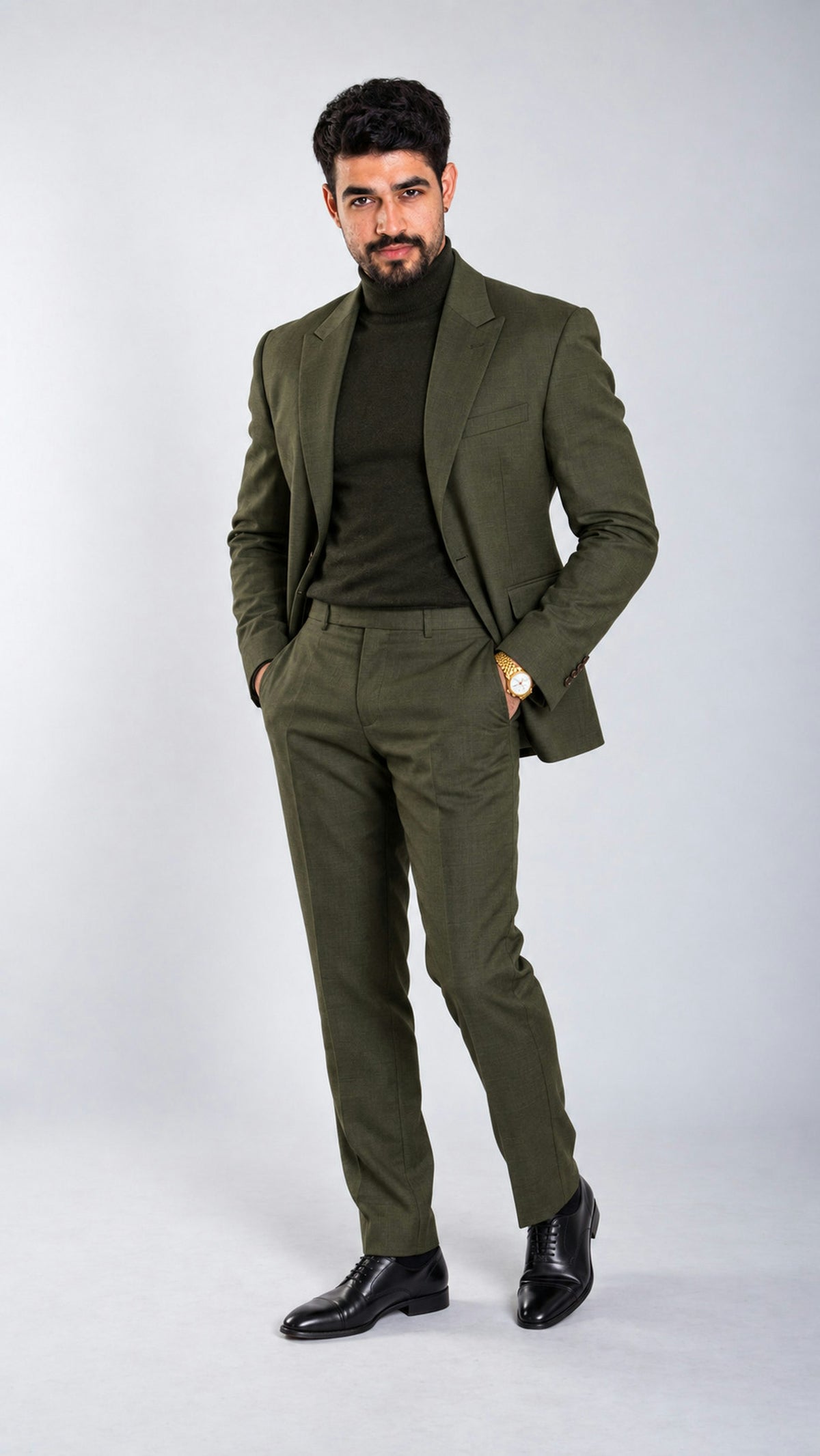 Hombre con saco y pantalón de lana verde olivo y suéter negro de cuello alto, en un estudio claro.